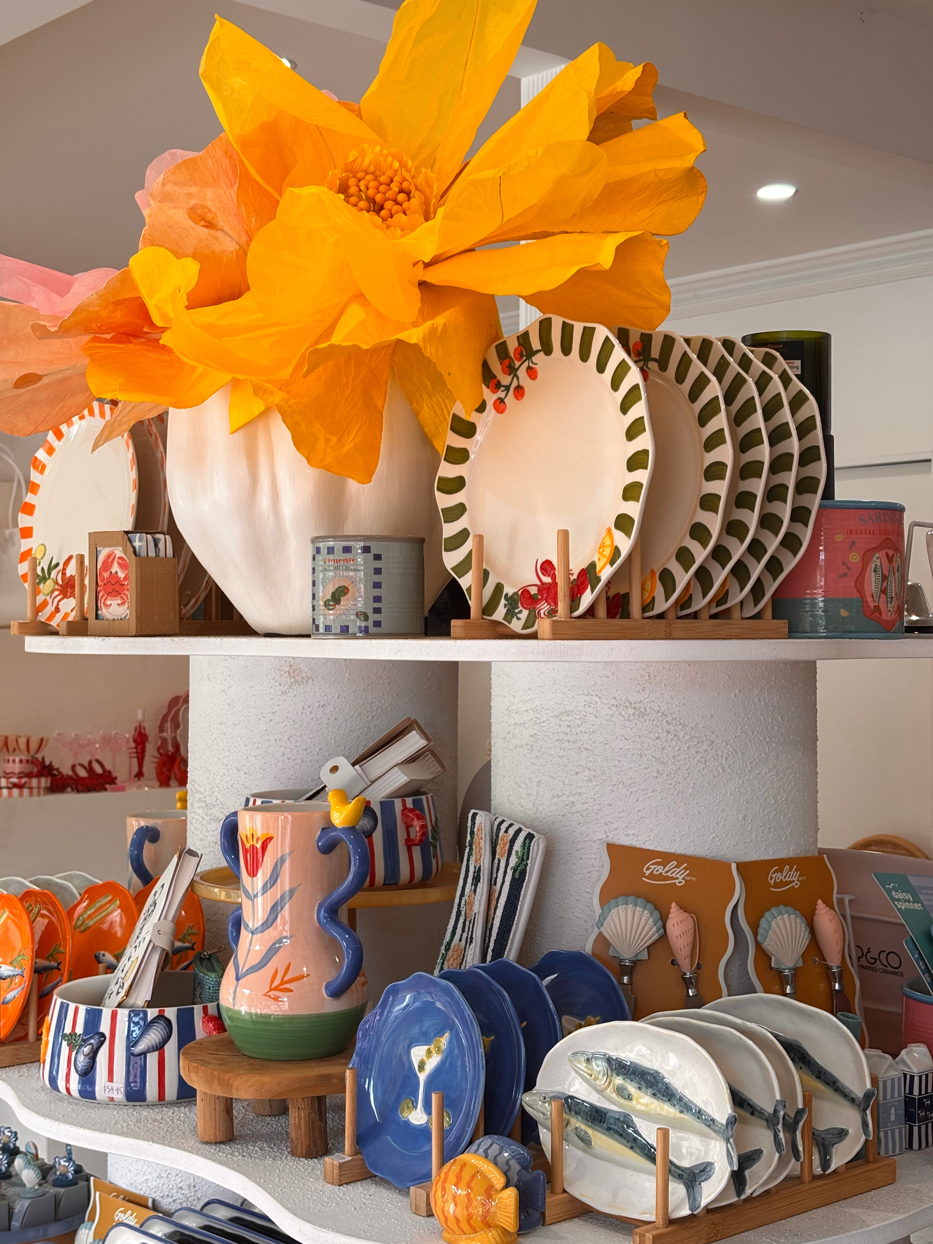 Display of ceramic plates, vases, and decorative items on shelves with a large orange flower.